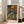 May include: Framed art print of a colorful self-portrait showing a bald man with mustache and beard in Post-Impressionist style, featuring vibrant oranges, greens, and blues. The wooden-framed poster leans against a white wall next to a beige sofa in a bright, minimalist living room with large windows and natural lighting.