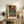May include: Framed reproduction of Matisse's self-portrait showing a bald man with white beard in vibrant colors - oranges, blues, and greens - displayed on rustic wooden sideboard alongside potted fern, ceramic vase, books, and leather chair in neutral-toned living room setting