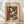 May include: Framed Henri Matisse poster print leaning against white wall on wooden floor. Abstract artwork features geometric shapes in vibrant colors - orange, green, red, blue, and white forms suggesting a figure wearing a hat. Natural wood frame with cream matting. Soft plant shadows cast on wall from window light.