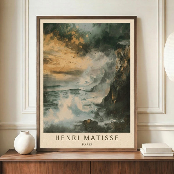 May include: Framed poster displaying a dramatic seascape with stormy clouds, rocky cliffs, and turbulent waves in muted greens, grays, and warm orange tones. Birds fly across the moody sky. Text reads "HENRI MATISSE PARIS" below the artwork. The brown-framed print sits on a wooden console beside a white ceramic vase and stacked books against cream walls with white molding.
