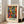 May include: Framed art print featuring vibrant abstract figures in flowing, dancing poses rendered in bold colors of orange, green, blue, purple and yellow with black silhouetted heads. The poster displays "MATISSE" in green text below the artwork and sits in a light wood frame against white walls near a beige upholstered sofa in a bright, naturally-lit room with large windows.