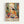 May include: Framed art poster featuring colorful Matisse-style painting of woman in yellow top sitting at table with fruit bowl, teacup, and red roses in blue vase. Vibrant interior scene with decorative patterns, plants, and warm tones throughout. Light wood frame against white wall.