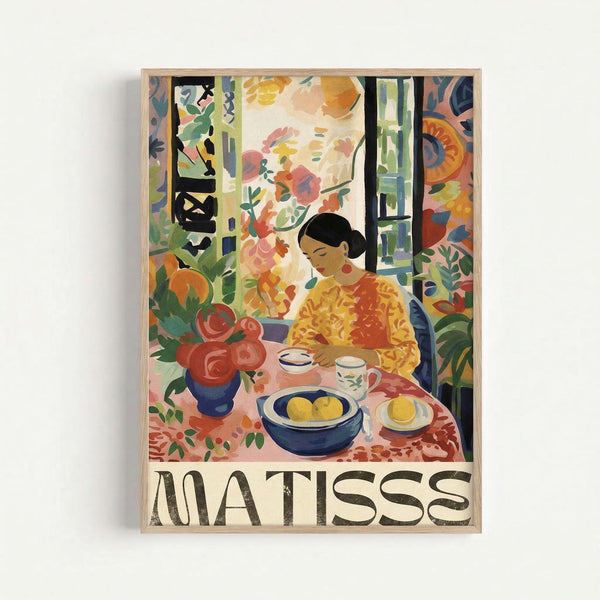 May include: Framed art poster featuring colorful Matisse-style painting of woman in yellow top sitting at table with fruit bowl, teacup, and red roses in blue vase. Vibrant interior scene with decorative patterns, plants, and warm tones throughout. Light wood frame against white wall.