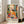 May include: Colorful Matisse-style poster in light wood frame leaning against white wall next to beige couch. Artwork shows figure in yellow top at table with blue bowl, flowers, and tea setting surrounded by vibrant floral patterns in oranges, greens, and reds. Modern living room with hardwood floors and large windows.