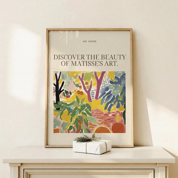 May include: Framed art poster featuring colorful abstract botanical design with green foliage, purple tree branches, yellow and orange circular shapes on cream background. Text reads "Discover the beauty of Matisse's art." Natural wood frame displayed on light wooden surface with small white wrapped gift beside it against cream wall.