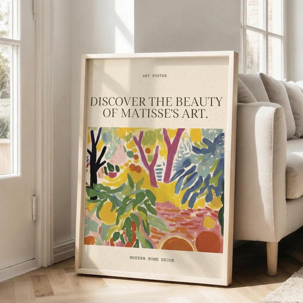 May include: Framed art poster displaying a vibrant Matisse-style garden scene with colorful abstract foliage, trees, and botanical elements in yellows, greens, blues, and coral tones. The poster features text reading "DISCOVER THE BEAUTY OF MATISSE'S ART" and "MODERN HOME DECOR" on cream background. Shown leaning against white wall next to beige upholstered chair in bright, naturally-lit room with white wood floors.