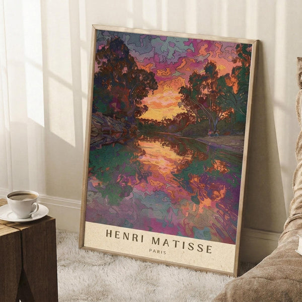 May include: Framed art print leaning against white wall showing vibrant landscape with trees, water reflection, and colorful sky in purple, orange, and green tones. Print features artist name at bottom. Scene includes coffee cup on wooden surface and textured white rug.