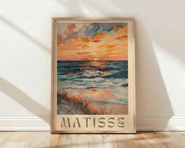 May include: Framed poster print featuring an impressionist seascape painting with vibrant orange sunset sky, turbulent blue-green ocean waves, and sandy beach with tall grass in foreground. The artwork shows expressive brushstrokes in warm oranges, cool blues, and earth tones. Text reading "MATISSE" appears below the image. Light wood frame sits against white textured wall on natural wood flooring with soft natural lighting casting shadows.