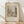 May include: Framed vintage botanical illustration print in light wood frame, leaning against white textured wall on wooden floor. The sepia-toned artwork depicts a peaceful riverside scene with trees, water, and a small structure. Soft natural lighting creates diagonal shadows across the minimalist setting. The print shows detailed pencil or etching style work typical of late 19th century landscape art.