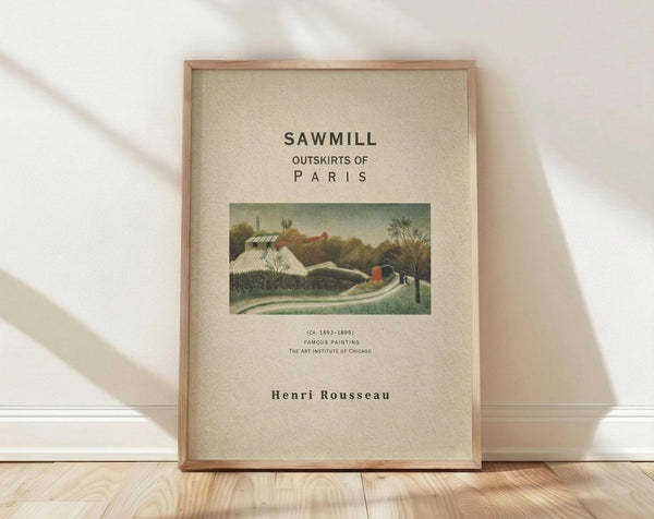 May include: Framed art print featuring Henri Rousseau's pastoral painting of a sawmill with white buildings, green fields, and trees. The poster has beige background with black text displaying the title, dates, and artist name. Shown in thin wooden frame leaning against white wall on light wood floor with soft natural lighting creating shadows.