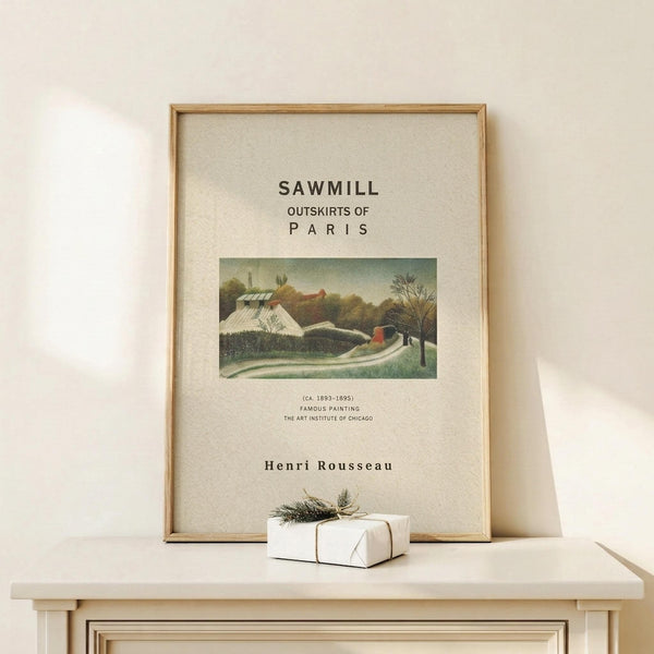 May include: Framed art print featuring Henri Rousseau's Sawmill painting with rustic buildings and green landscape, displayed on light wood shelf beside small wrapped gift with twine and pine sprig. Print has cream background with black text and natural wood frame against white wall.
