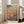 May include: Framed poster featuring abstract orange and pink polka-dotted spherical forms against a muted green background, displayed on wooden floor next to beige sofa in bright sunlit room with white walls and windows. Japanese text visible at top and bottom of artwork in cream-colored frame.