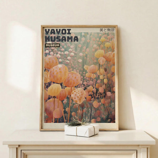 May include: Framed art print featuring colorful polka-dotted spherical sculptures on stems in orange, pink, and yellow tones against a muted background. The poster displays "YAYOI KUSAMA MUSEUM" text with Japanese characters. Set in a minimalist room scene with light wood frame, positioned on a white wooden surface next to a small wrapped gift box with natural twine and greenery accent.