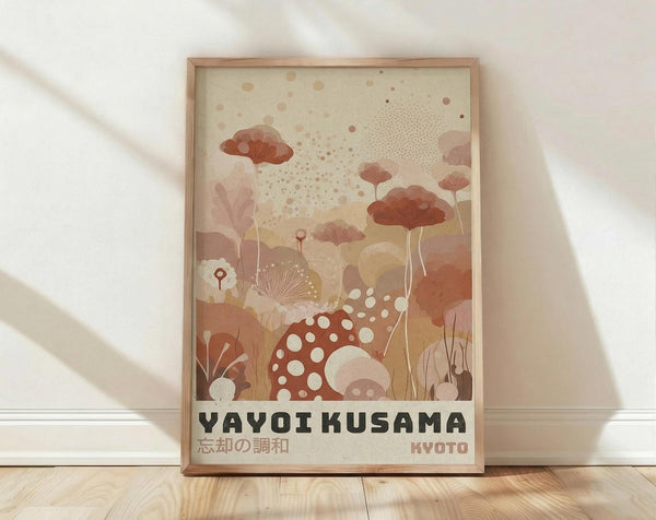 May include: Framed art print leaning against white wall on light wood floor. The poster features abstract botanical illustration in warm terracotta, peach, and cream tones showing stylized mushrooms, flowers, and organic shapes with polka dot patterns. Text reads "YAYOI KUSAMA" and "KYOTO" in black letters at bottom. Natural wood frame catches soft window light creating gentle shadows on white fabric backdrop.