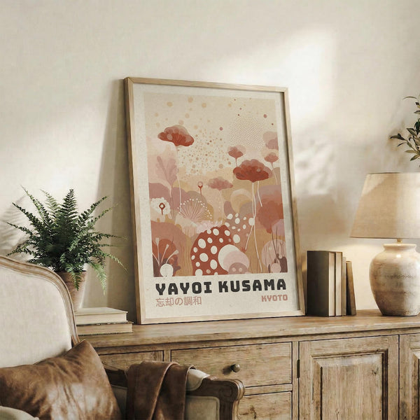 May include: Framed art print displayed on rustic wooden sideboard in warm-toned living room setting. Print features abstract botanical illustration with coral, pink and cream colors showing stylized mushrooms, flowers and organic shapes with polka dot patterns. Japanese text visible at bottom. Natural wood frame complements earth-toned decor including potted fern, ceramic vases, books, and beige upholstered furniture with throw pillows.