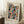 May include: Framed poster with colorful polka dot pattern in blues, oranges, yellows and teals on black background, leaning against white wall. Text reads "YAYOI KUSAMA" and "OSAKA 1988" with Japanese characters below. Light wood frame, displayed on white textured rug next to coffee cup on wooden box and beige fabric chair.