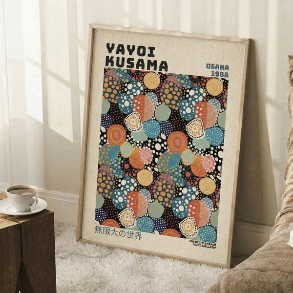 May include: Framed poster with colorful polka dot pattern in blues, oranges, yellows and teals on black background, leaning against white wall. Text reads "YAYOI KUSAMA" and "OSAKA 1988" with Japanese characters below. Light wood frame, displayed on white textured rug next to coffee cup on wooden box and beige fabric chair.