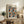 May include: Framed art poster with colorful polka dot pattern in blues, oranges, and earth tones displayed on rustic wooden sideboard. Room features neutral walls, potted fern, ceramic vase, stacked books, and brown leather armchair. Natural lighting creates warm, cozy living space atmosphere.