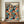 May include: Framed poster with colorful polka dot pattern in vibrant blues, oranges, reds and yellows on black background, displayed on wooden credenza next to white ceramic vase and books. The artwork features overlapping circles with dotted textures in Kusama's signature style, with "YAYOI KUSAMA" and "OSAKA 1988" text at top, Japanese characters at bottom. Cream colored walls and elegant interior setting visible.