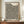May include: Framed exhibition poster with bold black text "YAYOI KUSAMA" and dense pattern of black polka dots on cream background, displayed on wooden sideboard next to white ceramic vase and books. Warm neutral room with paneled walls and natural lighting creates minimalist modern aesthetic.