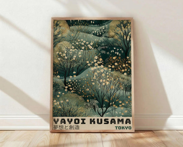 May include: A framed art print leaning against a white wall on light wood floors. The poster features an abstract botanical pattern in deep greens and sage tones with delicate white and cream flowers scattered throughout organic, flowing shapes. Bold black text reads "YAYOI KUSAMA" with Japanese characters below and "TOKYO" in the corner. The artwork is displayed in a natural wood frame, with soft natural lighting creating gentle shadows on the white fabric backdrop.