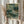 May include: Person holding framed art print featuring abstract botanical pattern in sage green and cream tones with dotted textures, small flowering branches, and Japanese text at bottom. Natural wood frame, shown with dried pampas grass against soft beige curtains in bright natural lighting.