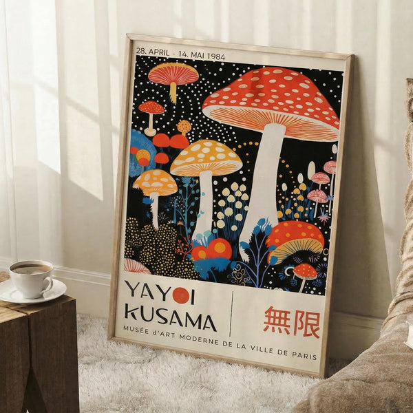 May include: Framed vintage-style exhibition poster featuring colorful mushrooms and fungi on black starry background, leaning against white wall corner next to small wooden side table with white coffee cup and saucer, cozy textured throw blanket visible at bottom right, natural window lighting creating soft shadows on white walls and fluffy area rug below.