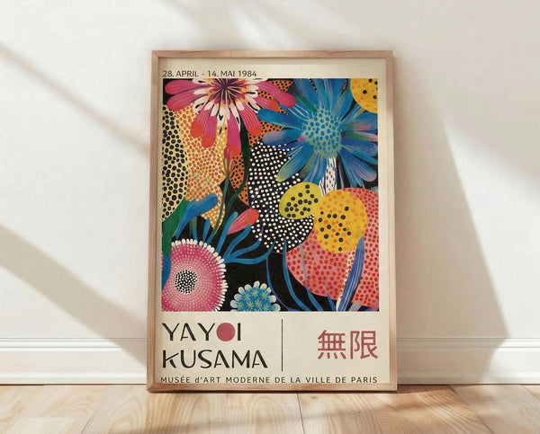 May include: Framed exhibition poster featuring vibrant floral artwork with polka dot patterns in pink, blue, yellow, and black. Shows stylized flowers and organic shapes with dotted textures characteristic of pop art style. Text reads "YAYOI KUSAMA" with Japanese characters and museum details, dated 1984. Natural wood frame leaning against white wall on light wooden floor with soft shadows.