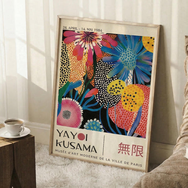 May include: Framed poster propped against white wall on textured rug beside wooden stool with coffee cup. Artwork features vibrant pop art style flowers in pink, blue, yellow, and orange with bold polka dot patterns. Text shows "YAYOI KUSAMA" and dates "28. APRIL - 14. MAI 1984" with "MUSÉE D'ART MODERNE DE LA VILLE DE PARIS" below colorful floral design.