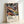 May include: Framed art print leaning against white wall showing abstract swirling patterns in vibrant colors including orange, blue, purple, yellow, and black with polka-dotted organic shapes and flowing lines. Text reads "YAYOI KUSAMA" with Japanese characters and "MUSÉE D'ART MODERNE DE LA VILLE DE PARIS" below the colorful psychedelic artwork in natural wood frame.