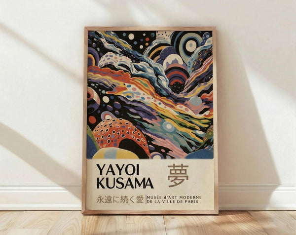 May include: Framed art poster featuring abstract swirling patterns in vibrant colors including orange, purple, blue, and yellow with polka dot elements. Text reads "Yayoi Kusama" with Japanese characters and "Musee d'Art Moderne de la Ville de Paris" below colorful psychedelic design. Natural wood frame displayed on light wooden floor against white fabric backdrop with soft shadows.