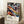 May include: Framed poster with vibrant abstract swirling patterns in blues, oranges, purples and yellows against black background, featuring polka dots and flowing organic shapes. Text reads "YAYOI KUSAMA" with Japanese characters and "MUSEE D'ART MODERNE DE LA VILLE DE PARIS" below. Natural wood frame leans against white wall next to white coffee cup on wooden surface and beige textured blanket on light carpet.
