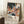 May include: Framed art poster leaning against white wall on fluffy white rug. Features colorful abstract design with cacti, flowing organic shapes, polka dots on black starry sky transitioning to warm coral and earth tones below. Text shows "YAYOI KUSAMA" and Japanese characters with museum credit. White coffee cup on wooden block nearby, beige throw blanket visible at edge.