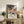 May include: Framed poster with abstract landscape featuring colorful cacti, flowing organic shapes, and polka dot patterns against a starry night sky. Japanese text visible at bottom. Displayed on rustic wooden sideboard beside fern plant, ceramic vase, and books in modern living room with beige armchair and neutral walls.