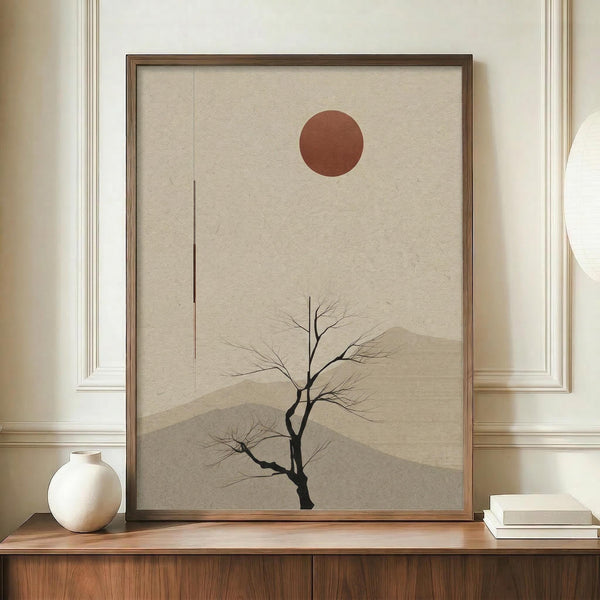 May include: Framed minimalist artwork featuring a bare black tree silhouette against beige textured background with terracotta sun and layered mountain shapes, displayed on walnut wood sideboard beside white ceramic vase and stacked books in neutral-toned room with white paneled walls.