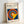 May include: Framed poster with cream mat featuring colorful concentric circles in red, yellow, blue, and orange on navy background. Yellow triangular shape intersects the circles. Text reads "BAUHAUS Modernism, minimalism & abstract arts 1919-1933" and "SCHOOL OF ARCHITECTURE WEIMAR, DESSAU, BERLIN". Light wood frame leans against white wall on light surface.