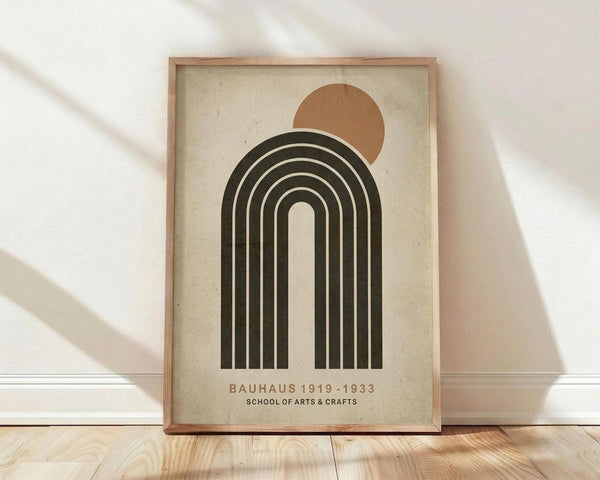 May include: Framed poster with geometric design featuring concentric black arches beneath a rust-colored circle on cream textured paper, displayed in light wood frame leaning against white wall on wooden floor with soft natural lighting creating diagonal shadows