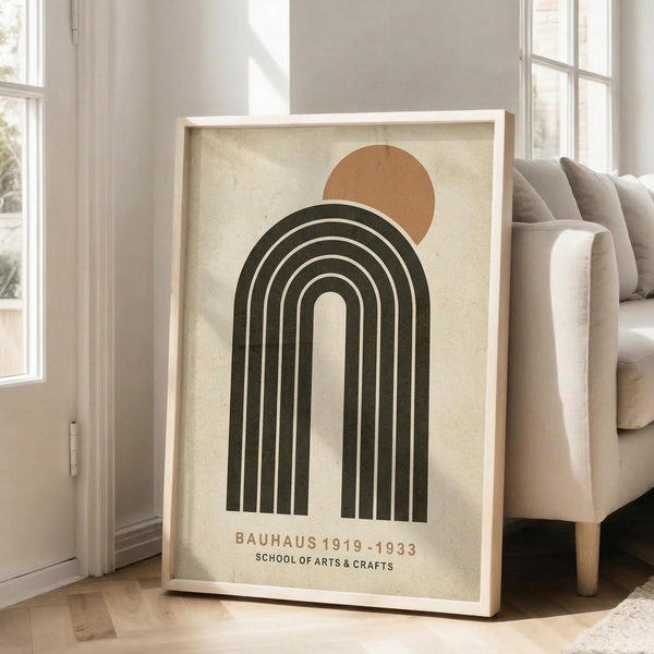May include: Framed poster featuring minimalist geometric design with dark green concentric arches and terracotta circle on cream textured background, displayed in light wood frame leaning against white wall next to beige upholstered sofa in bright modern living room with large windows and natural lighting.