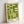 May include: Framed poster with olive green geometric design featuring angular shapes and lines on cream background, displayed in light wood frame leaning against white wall on light surface. Modern minimalist artwork with "bauhaus 1919" text in black at bottom corner.