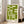 May include: Green geometric Bauhaus-style poster in light wood frame leaning against white wall in bright living room. Chunky beige sectional sofa with throw pillows visible to right. White window frames with natural light streaming in. Hardwood floors with area rug. Poster features bold lime green angular shapes on cream background with "bauhaus 1919" text at bottom.