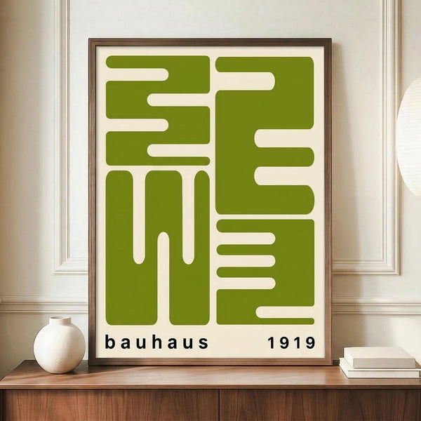 May include: Framed geometric poster with olive green interlocking shapes forming maze-like pattern on cream background, displayed on wooden sideboard next to white ceramic vase and stacked books in elegant room with white wainscoting and warm lighting.