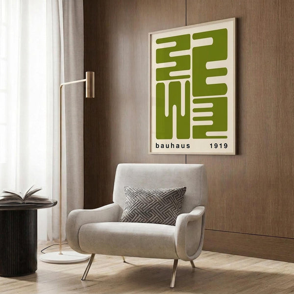 May include: Green geometric poster with white linear pattern in light wood frame, displayed on wood-paneled wall above light gray upholstered armchair with geometric throw pillow, alongside brass floor lamp and dark round side table with open book