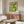 May include: Green geometric Bauhaus poster with white background and "bauhaus 1919" text, displayed in thin wooden frame above walnut credenza. Modern living room setting with cream curved chair, glass oval coffee table, white table lamp, and copper floor lamp. Sunlight creates shadows on light walls.