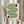 May include: Person in cream sweater holding framed geometric art print featuring flowing green and black striped wave pattern with circular accents, displayed against neutral curtained background with dried pampas grass bundle, showcasing minimalist Bauhaus-inspired design in natural wood frame