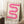 May include: Framed poster with pink gradient wavy ribbon design against cream background, displaying "bauhaus 1919" text below. Light wood frame leaning against white wall corner next to beige textured rug, wooden side table with white coffee cup, and tan fabric in soft natural lighting.