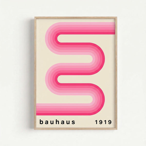 May include: Framed poster print hanging on white wall featuring a pink gradient ribbon design in flowing S-shaped curves with multiple layers transitioning from light to deep pink. Black text "bauhaus 1919" appears at bottom on cream background. Natural wood frame with thin profile.