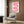 May include: Modern living room scene with beige armchair featuring geometric patterned pillow, gold floor lamp with white circular base, dark round side table with open book, and wood paneled wall displaying framed pink ribbon-shaped poster with gradient flowing curves and black text reading "bauhaus 1919" on cream background.