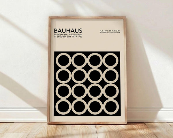 May include: Framed Bauhaus poster with cream background and black geometric pattern of white circles arranged in grid. Modern minimalist design in natural wood frame, leaning against white wall on light wooden floor with soft shadows.