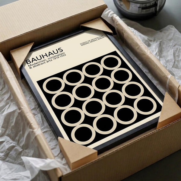 May include: Black and white geometric poster with repeating circles pattern in black frame, nestled in cardboard packaging with white tissue paper and wooden dowels for shipping protection, displayed on neutral surface