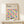 May include: Framed Bauhaus-inspired poster with colorful geometric circles in blues, yellows, oranges, and purples arranged in a grid pattern, displayed on light wood floating shelf against cream wall with small wrapped gift box beside it.